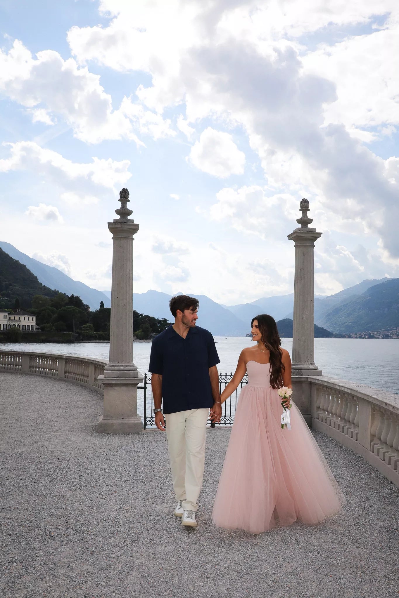 Couple holding hands on the lakeside promenade at Villa Melzi, bride-to-be in a flowing pink tulle dress
