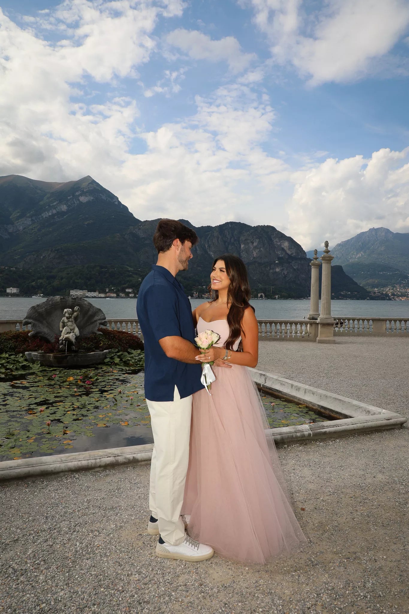 Bride-to-be in a blush tulle dress smiling at her fiancé on the lakeside terrace of Villa Melzi in Bellagio