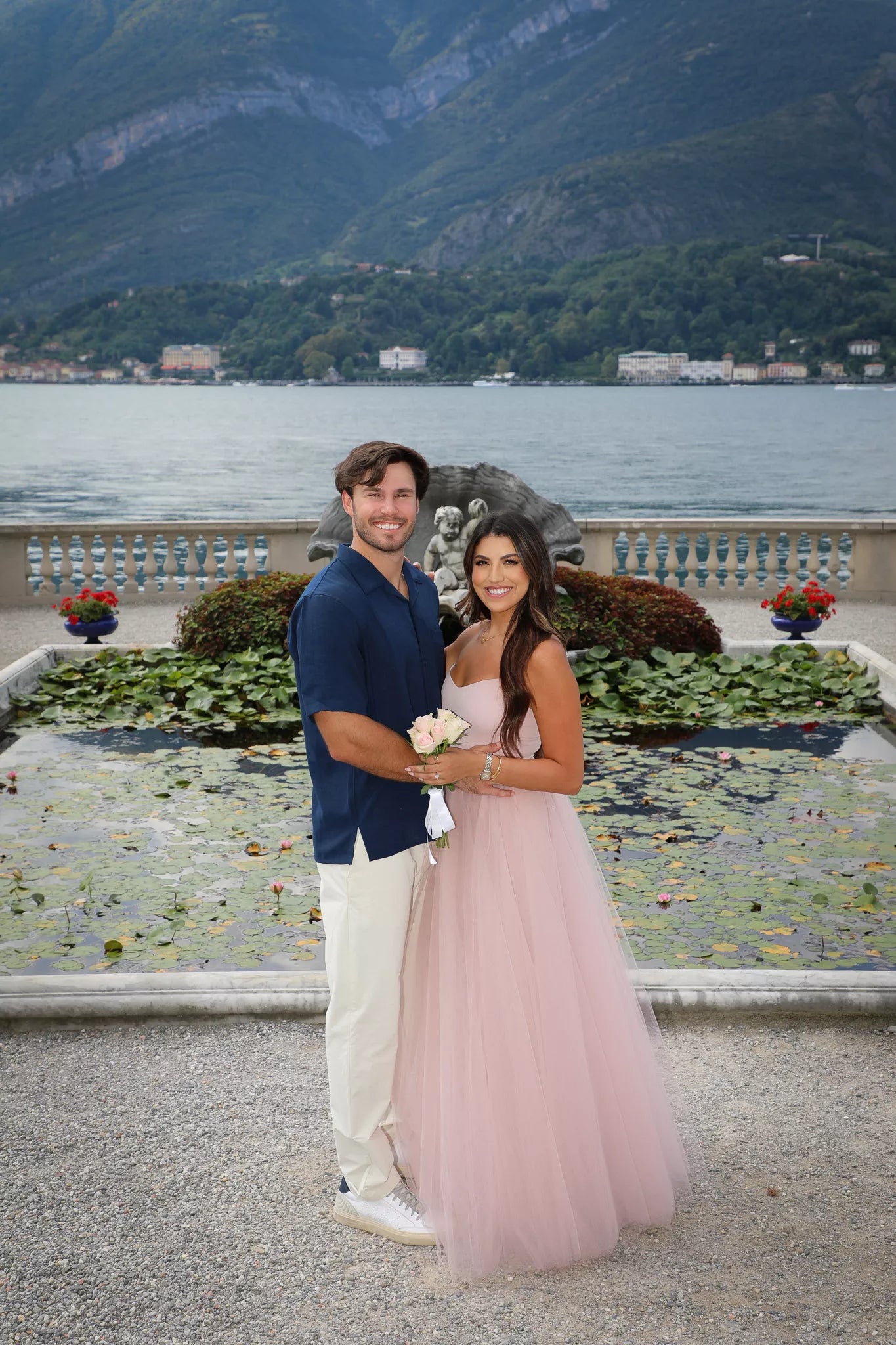 Couple standing in front of the lily pond with Lake Como and the Bellagio shoreline behind them at Villa Melzi gardens
