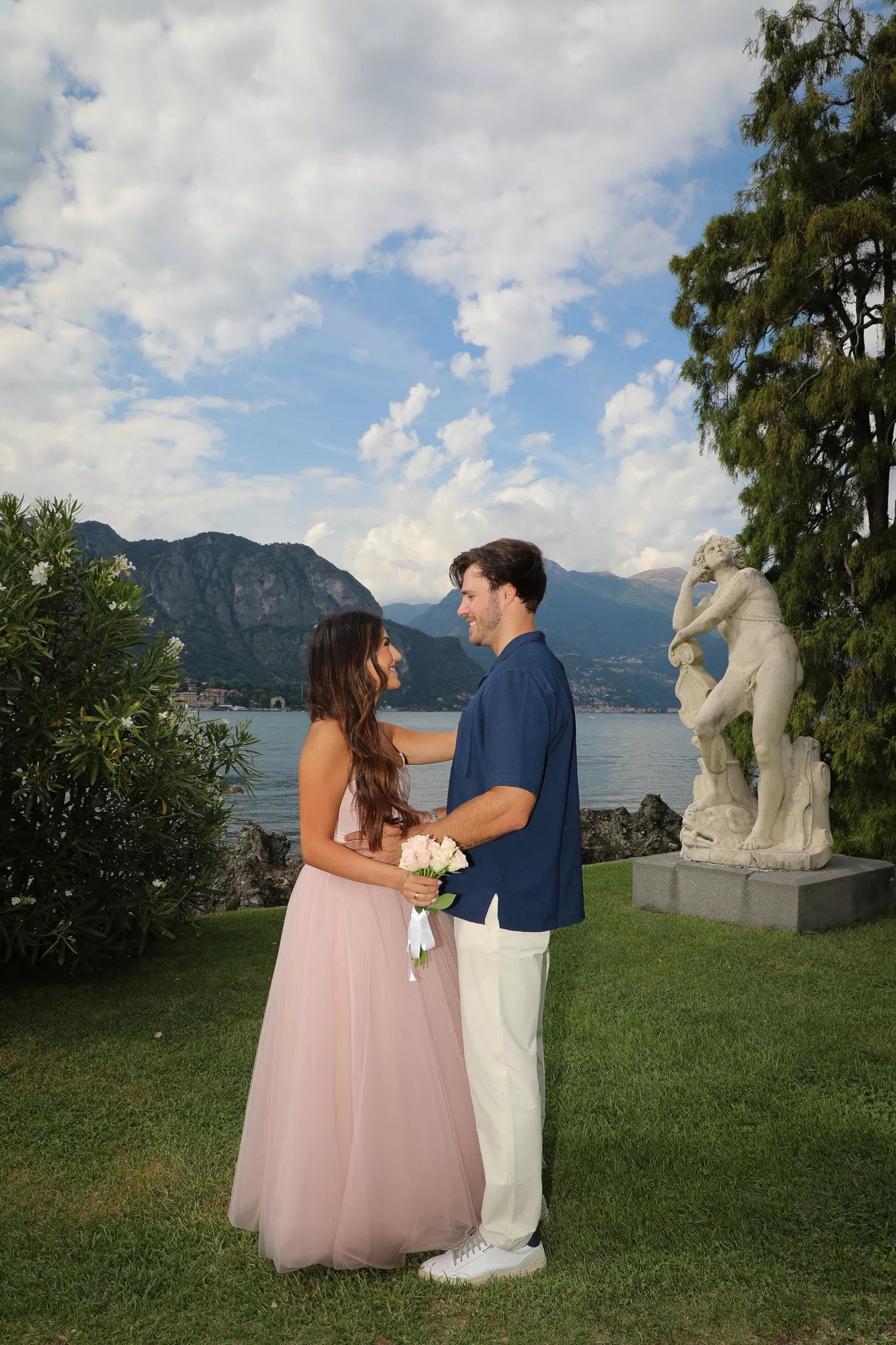 Couple facing each other in front of a classical statue in the lakeside gardens of Villa Melzi in Bellagio