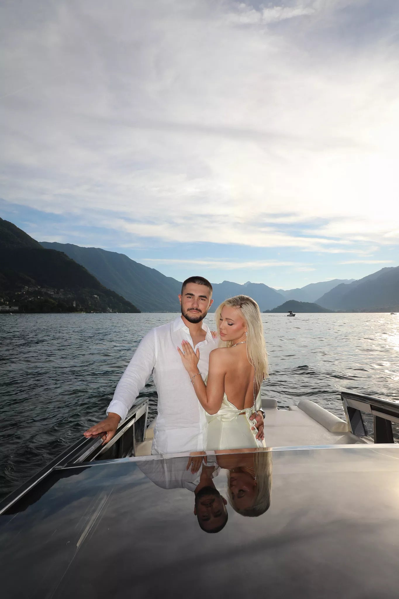 Elegant couple standing on a boat with their reflection on the deck and wide Lake Como views