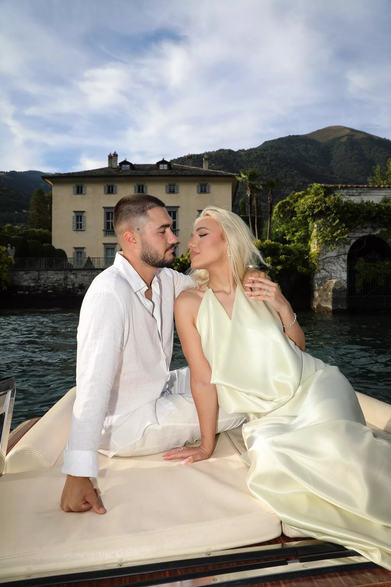 Couple relaxing on a boat deck with historic Lake Como villa and mountains in the background