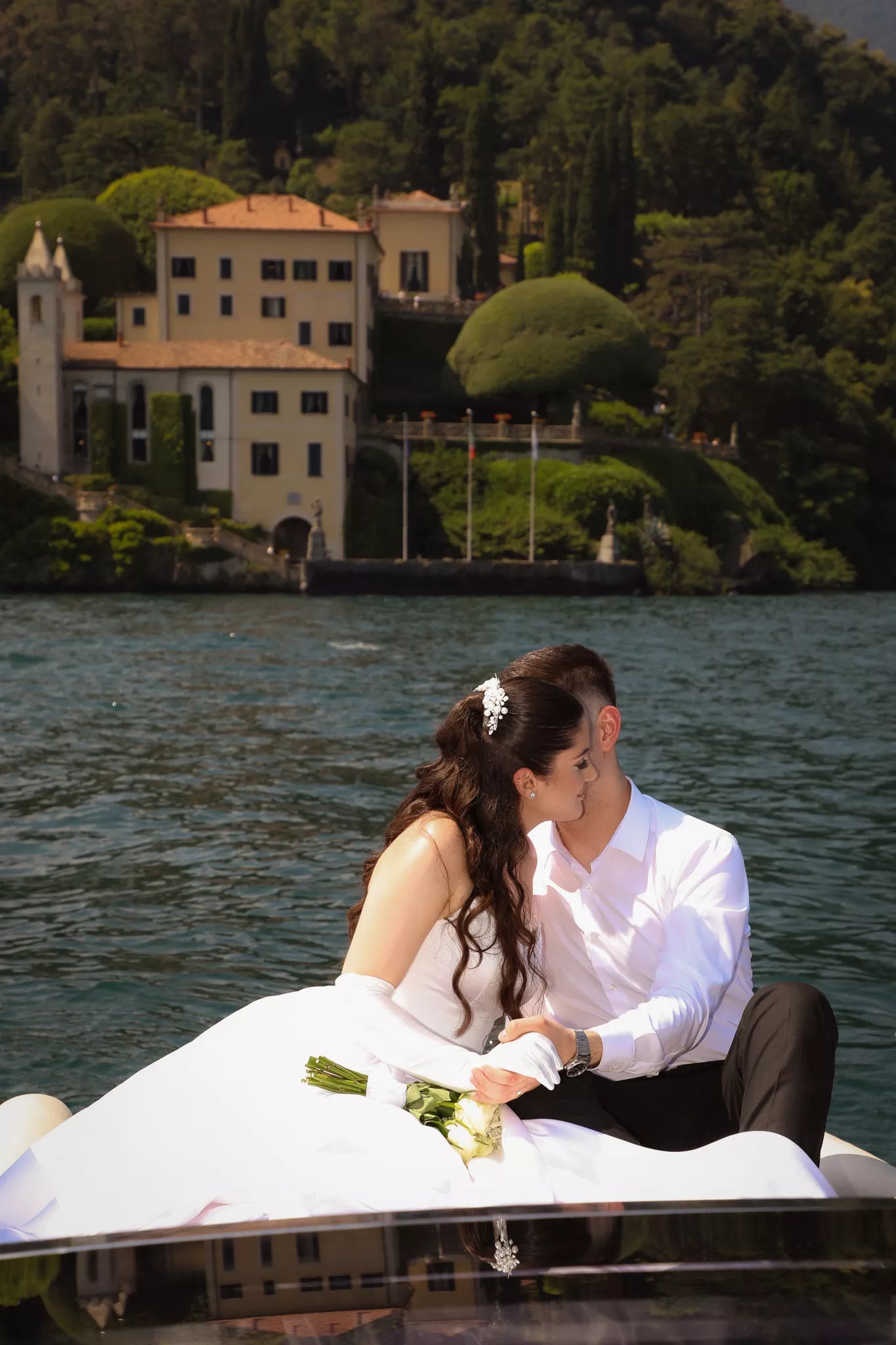 Bride and groom embracing on a private boat on Lake Como with a historic lakeside villa in the background