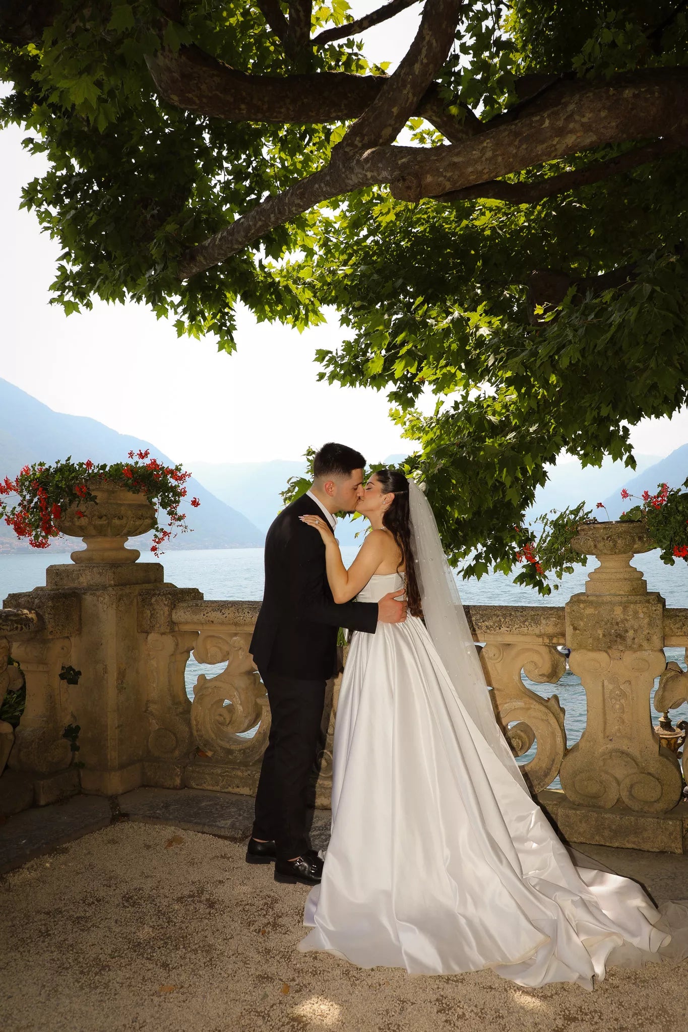Bride and groom kissing beneath a leafy tree on a Lake Como terrace during an intimate wedding portrait session
