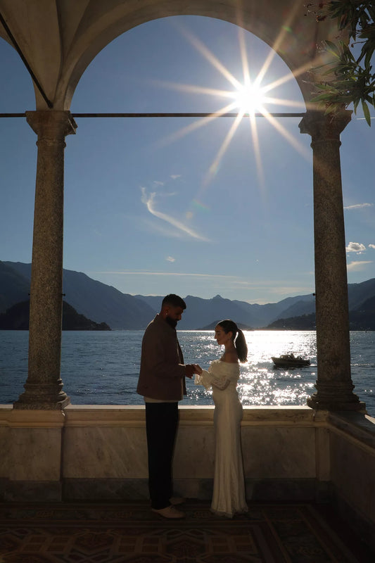 Couple exchanging rings under stone arches at Villa Monastero with Lake Como and sun flare in the background