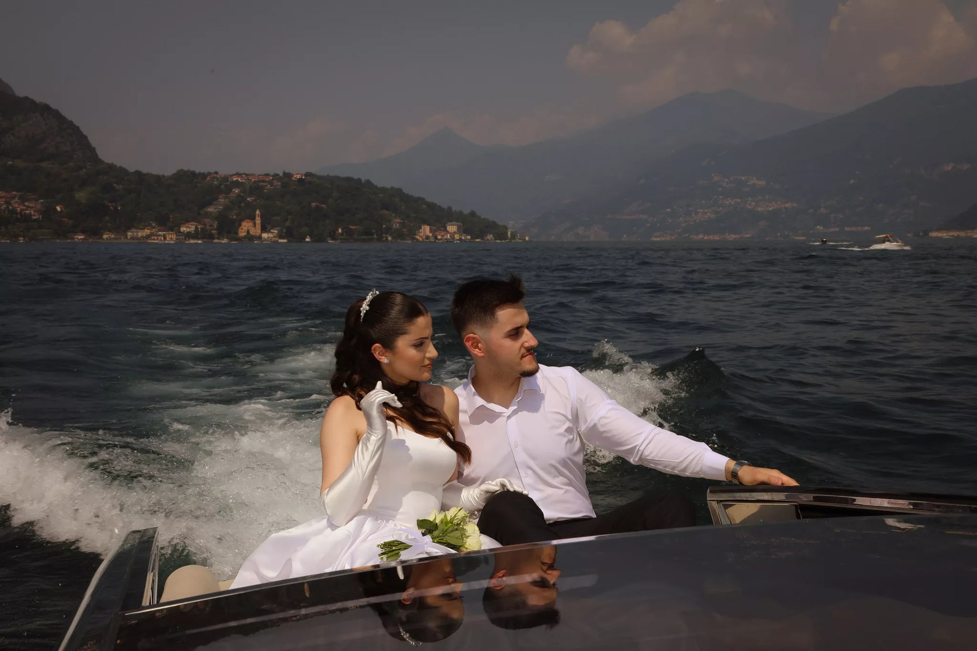 Wedding couple enjoying a stylish boat ride across Lake Como with open water, mountains and wake behind them