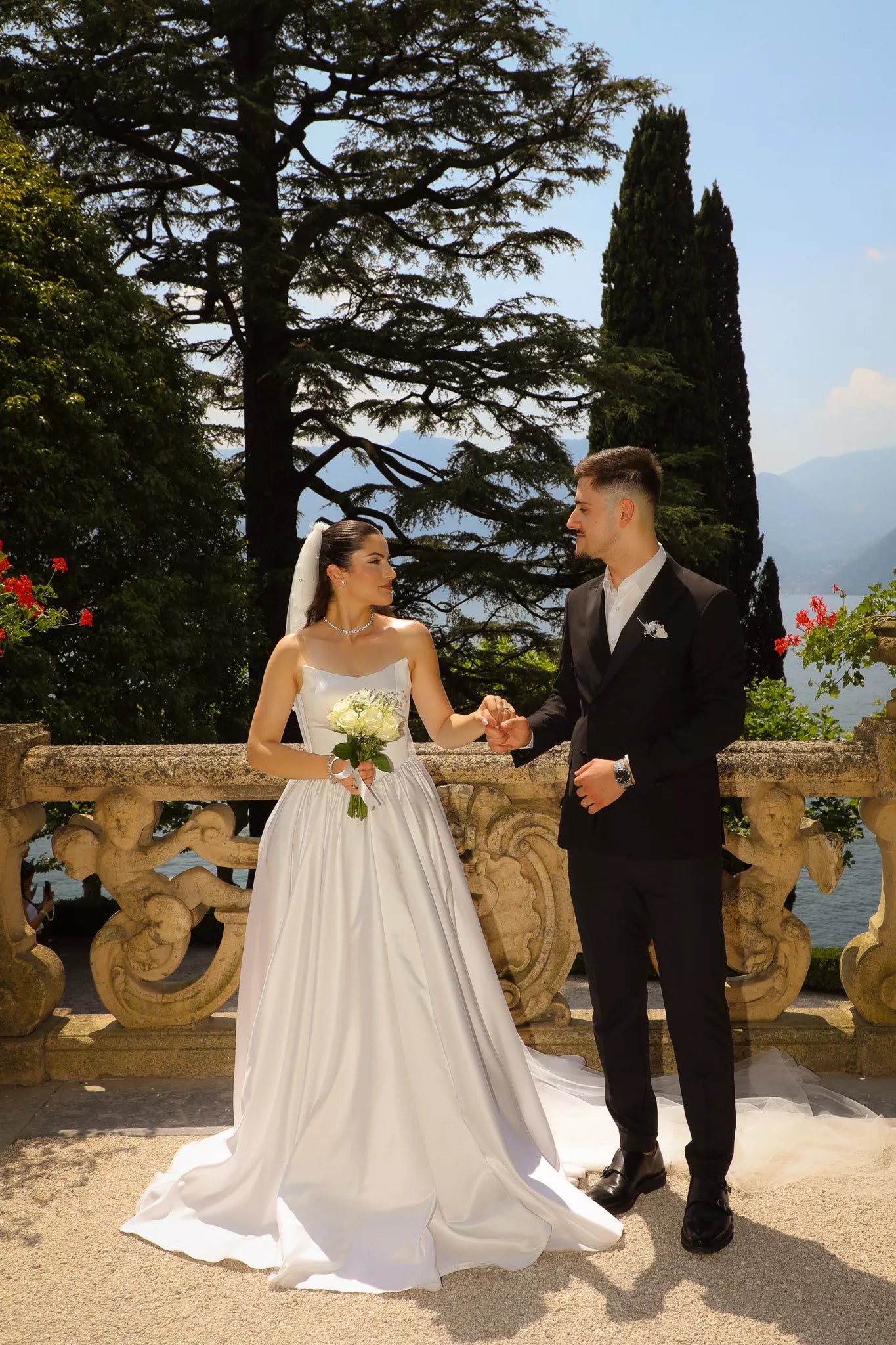 Elegant wedding couple holding hands on the historic terrace of Villa del Balbianello with lake views behind them