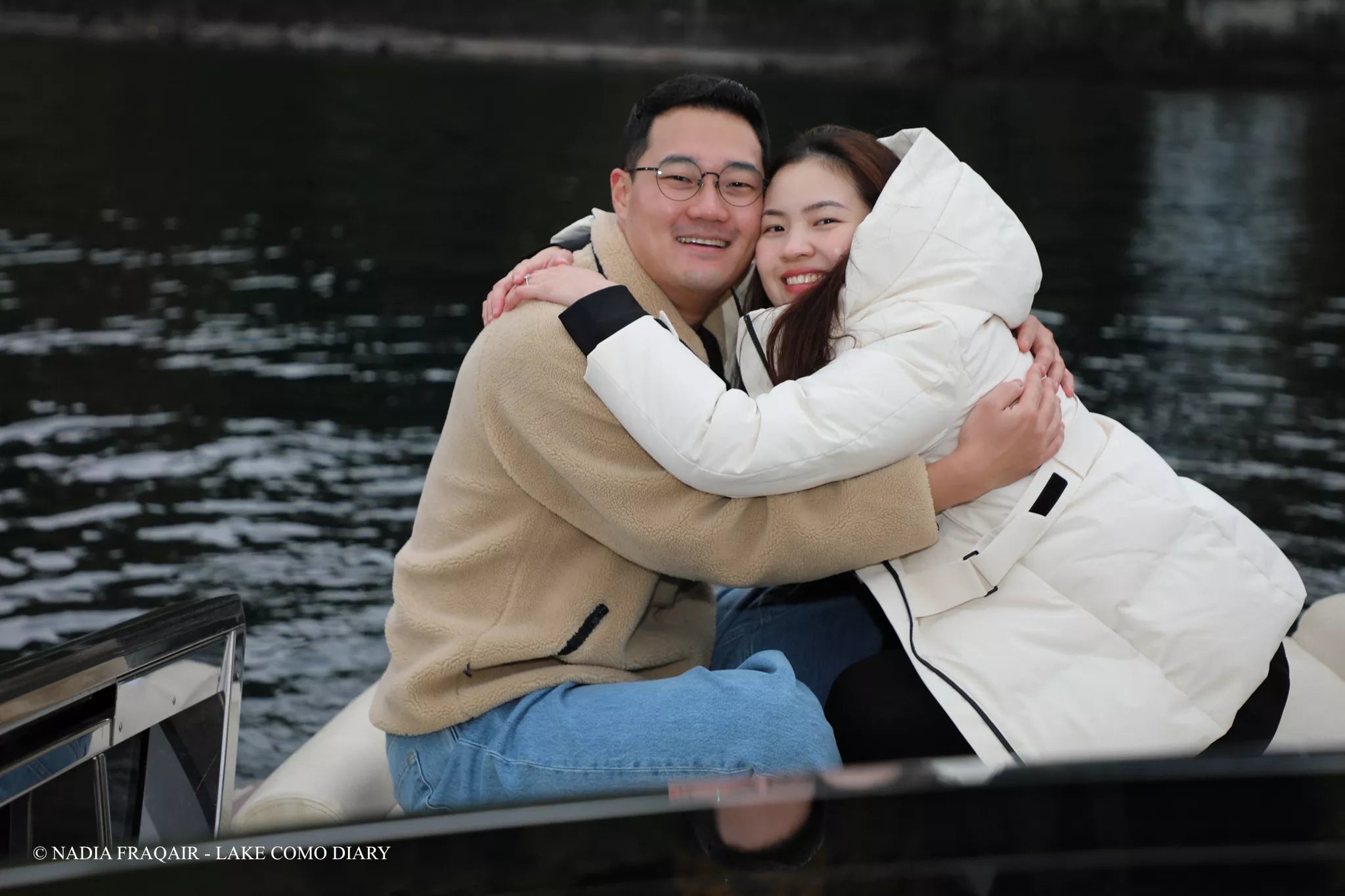 Couple wrapped in a warm embrace on a private boat in November on Lake Como — intimate proposal photography by Nadia Fraqair.