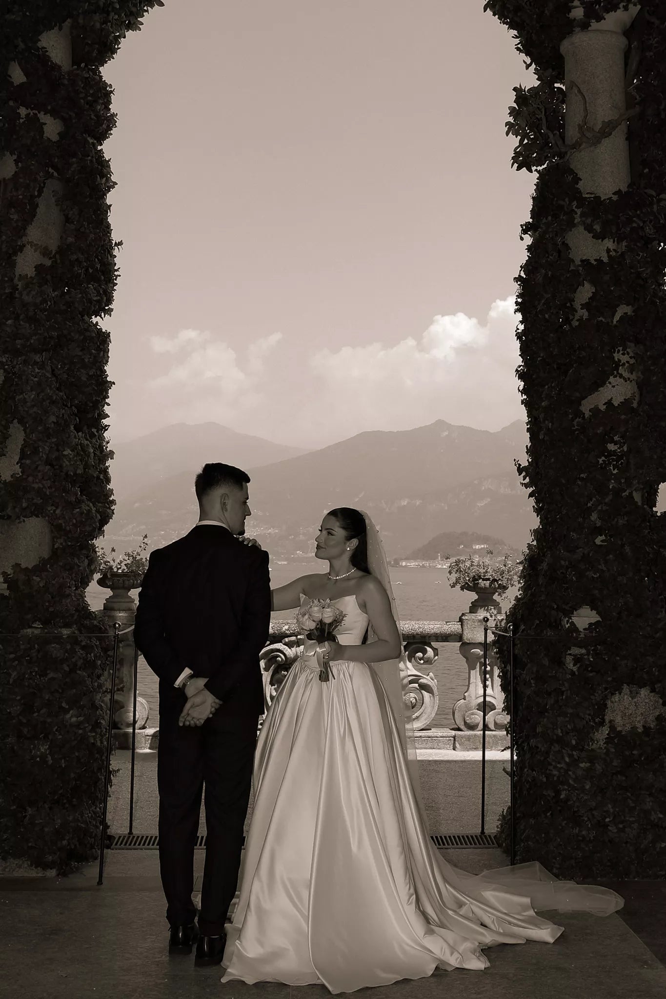 Sepia wedding portrait of a bride and groom framed by the ivy-covered archway at Villa del Balbianello