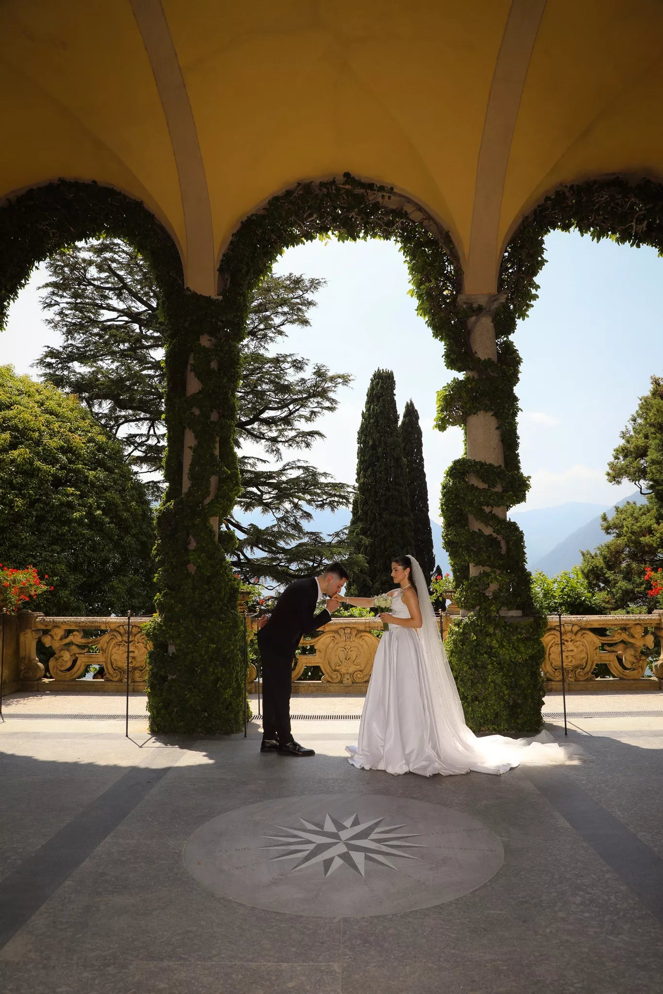 Groom kissing the bride’s hand under the elegant arches of Villa del Balbianello overlooking Lake Como