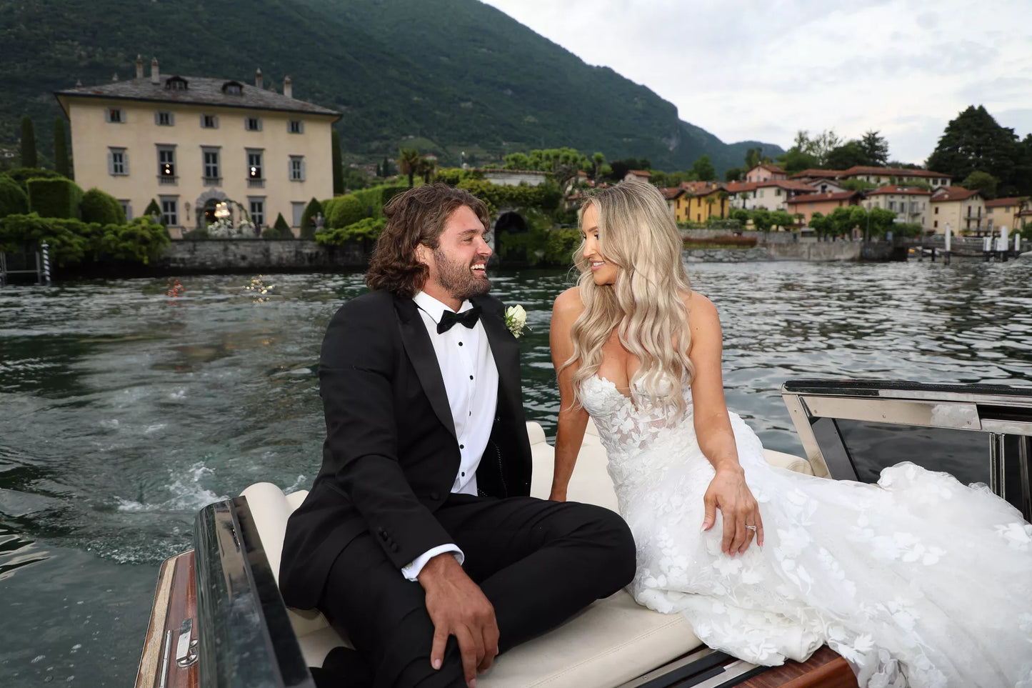 Lake Como wedding photography of bride and groom laughing together on a private boat with a lakeside villa in the background