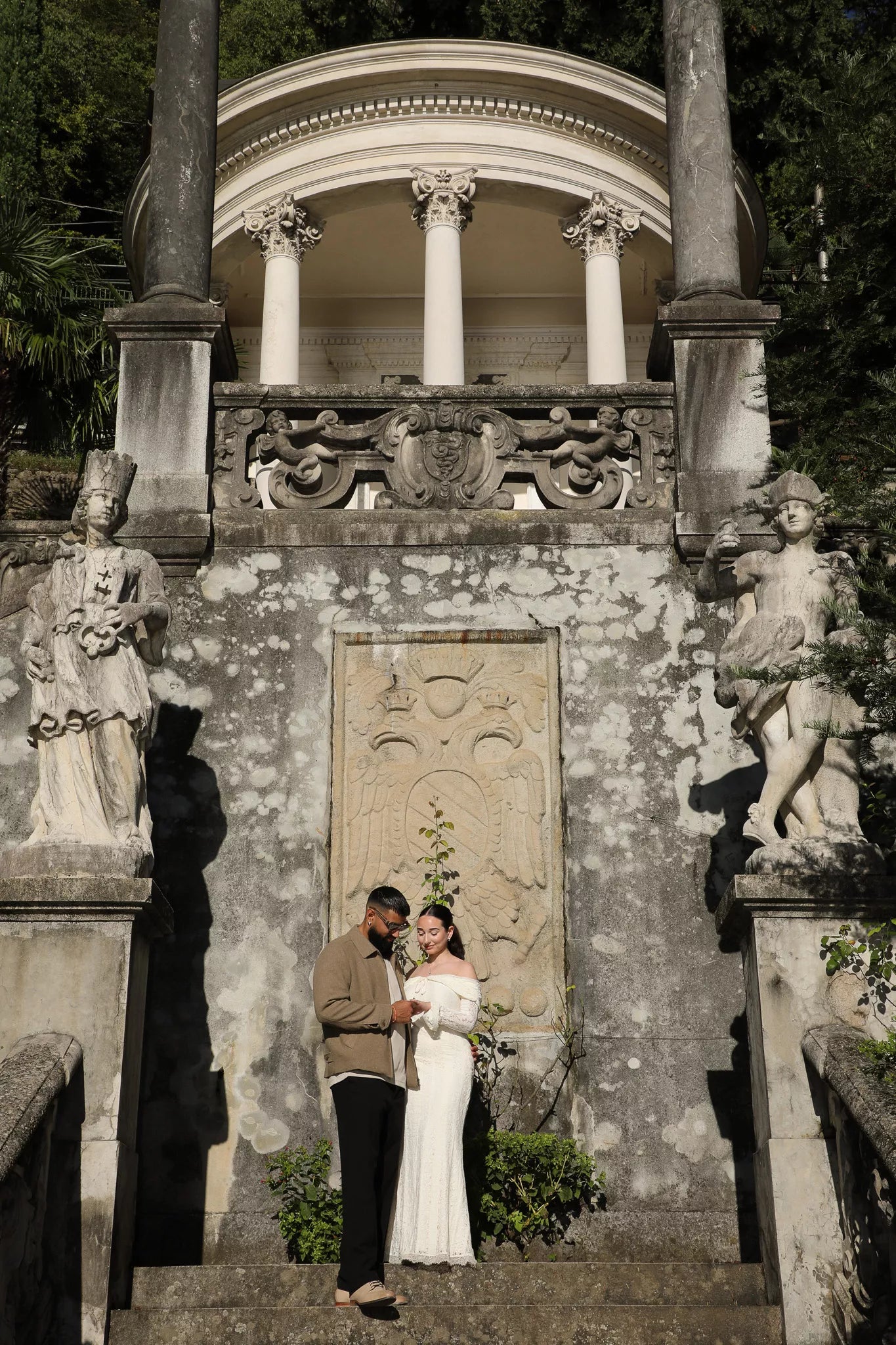 Couple standing on the stone staircase at Villa Monastero in Varenna with statues and a neoclassical pavilion, captured by a Lake Como wedding and proposal photographer